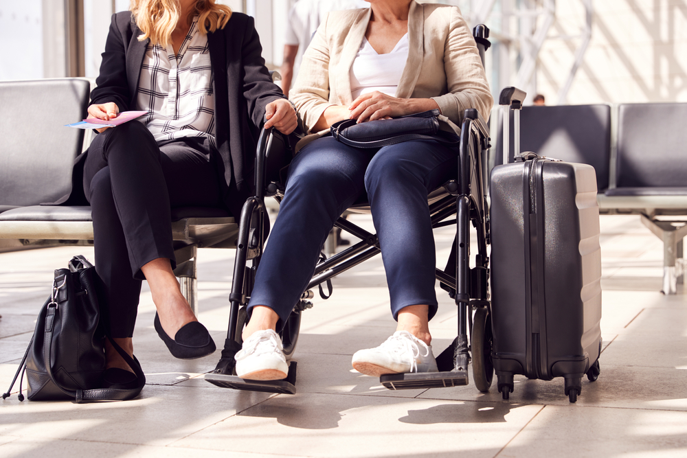 Woman in wheelchair sitting in airport with suitcase and female companion