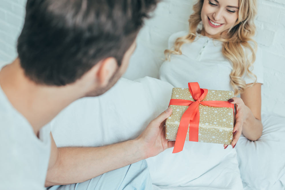 Young man handing wrapped present to woman in bed