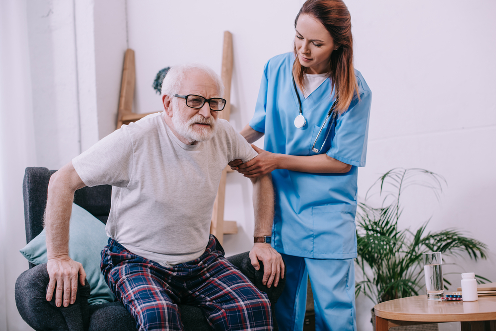 Nurse helping elderly man stand from armchair