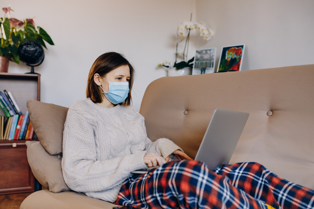 Woman wearing face mask using laptop on couch