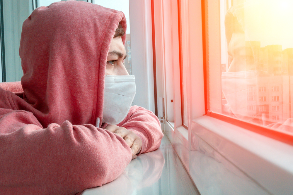 Man in hoodie and face mask looking out window