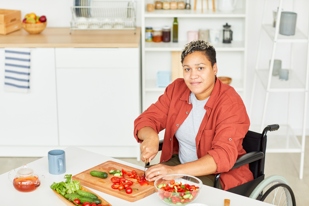 Woman in wheelchair chopping vegetables at low countertop
