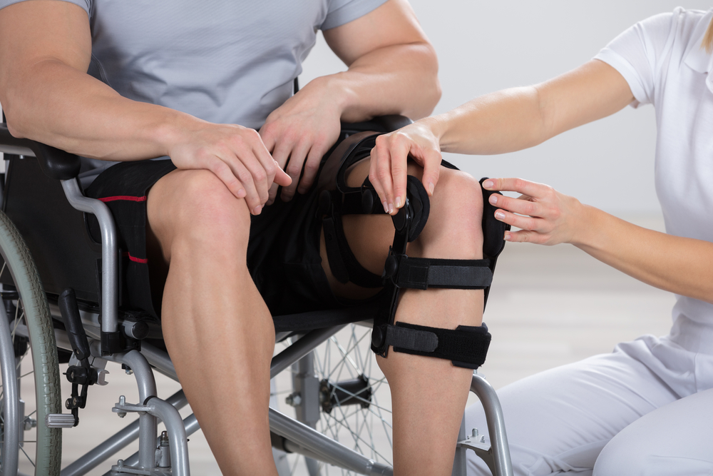 A nurse assisting a man in a wheelchair with his knee brace.