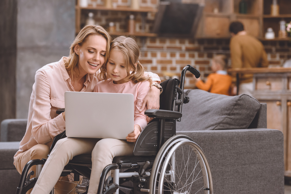 Little girl in wheelchair using laptop with her mother