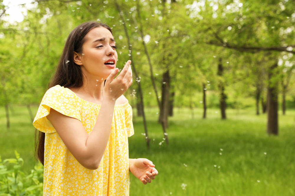 Young woman outdoors and surrounded by pollen about to sneeze
