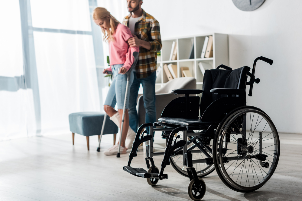 Woman using crutches near wheelchair