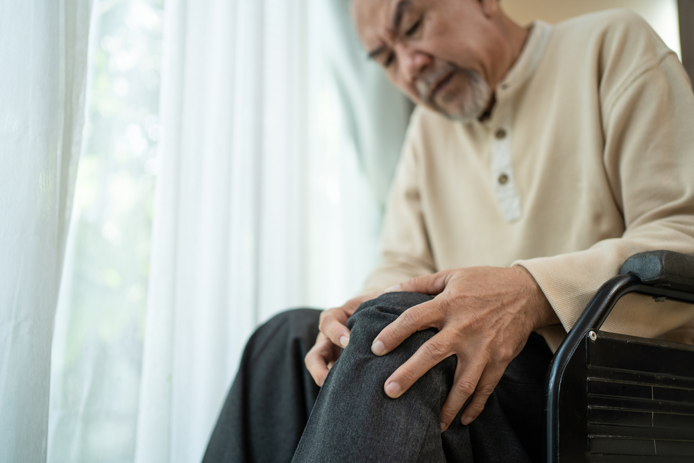 Elderly man in wheelchair massaging sore leg