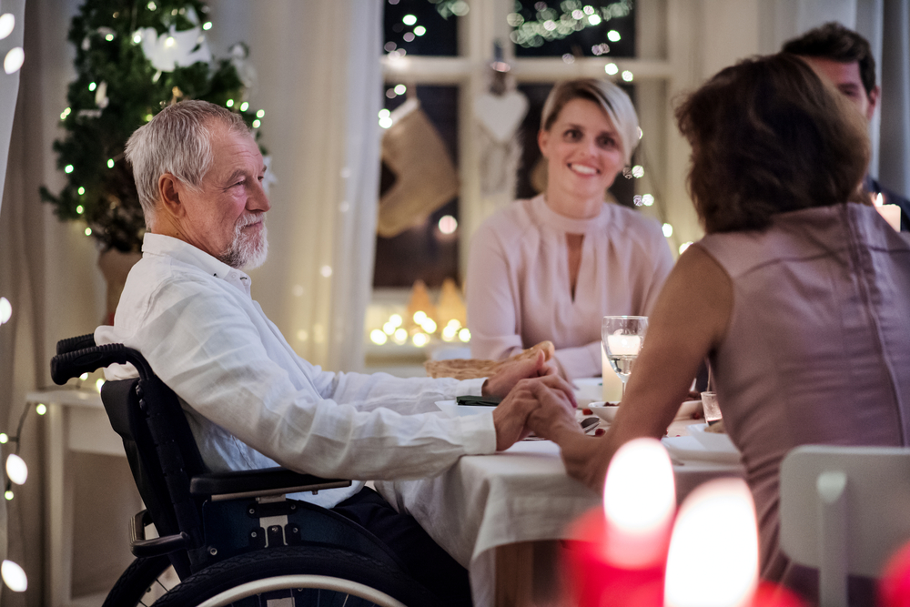 Senior man in wheelchair being pushed up to table at Christmas dinner