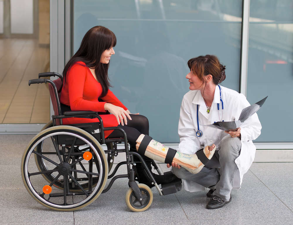 Woman sitting in a wheelchair with a cast on her leg while talking to a squatting doctor.