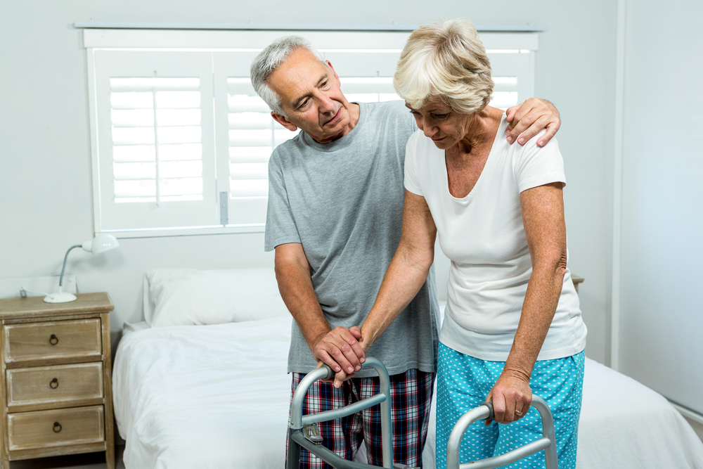 Elderly man helping woman use walker