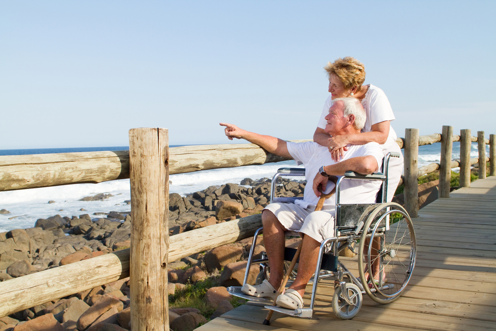 Senior man in wheelchair and senior woman on boardwalk at beach
