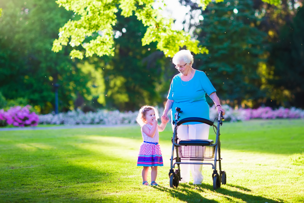 Elderly woman using a walker to stroll with a young girl outside.